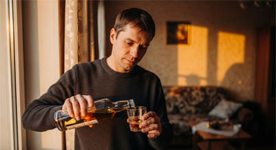 Мужчина у окна наливает алкоголь в стакан